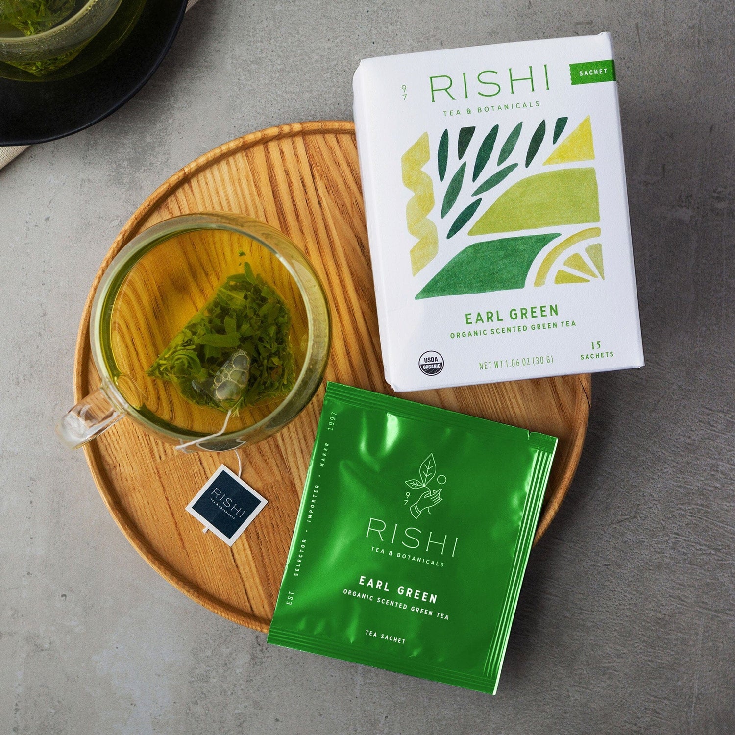 Rishi Earl Green tea packages with a glass of tea on a wooden tray.