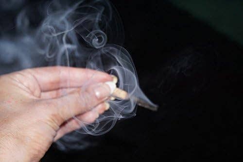 Hand holding a lit palo santo match with smoke against a dark background