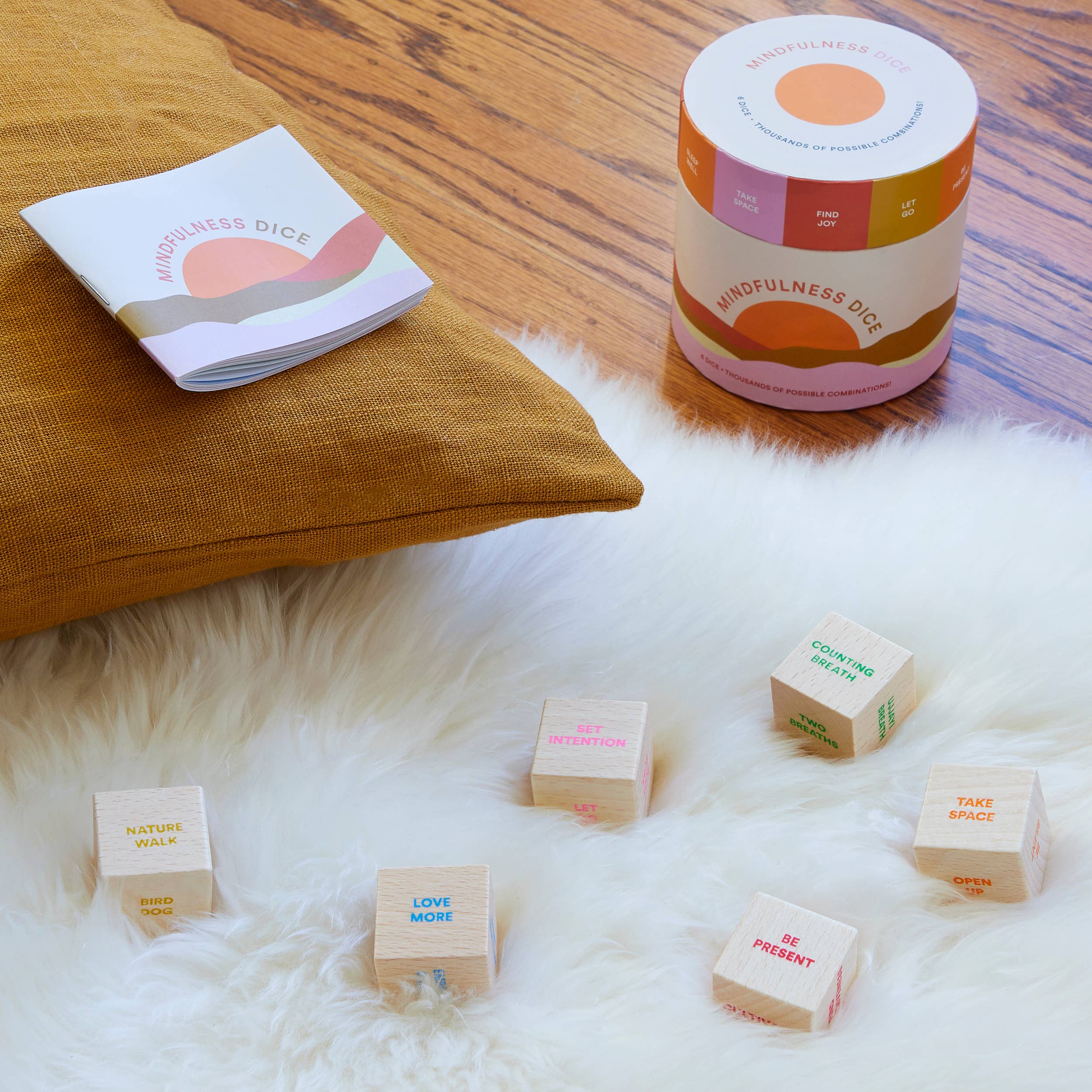 Wooden dice with text on a fluffy white surface next to a container labeled 'Mindfulness Dice' on a wooden floor.